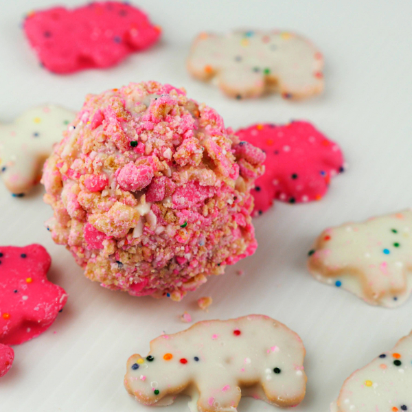 Our Animal Cracker Cake Ball starts with a classic vanilla cake, baked to perfection and then crumbled into fine pieces. We mix the cake crumbs with creamy frosting, roll them into bite-sized balls, and then dip them in a smooth, pink-hued chocolate coating. As a final touch, each cake ball is adorned with a crushed animal crackers, adding a playful crunch to this delightful dessert.