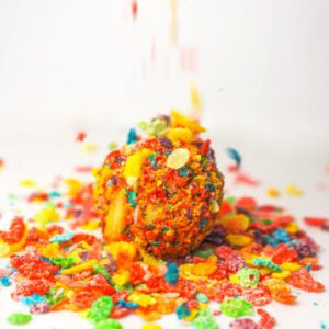 A vanilla bean cake ball bursting with colorful Fruity Pebbles cereal, dipped in smooth white chocolate.