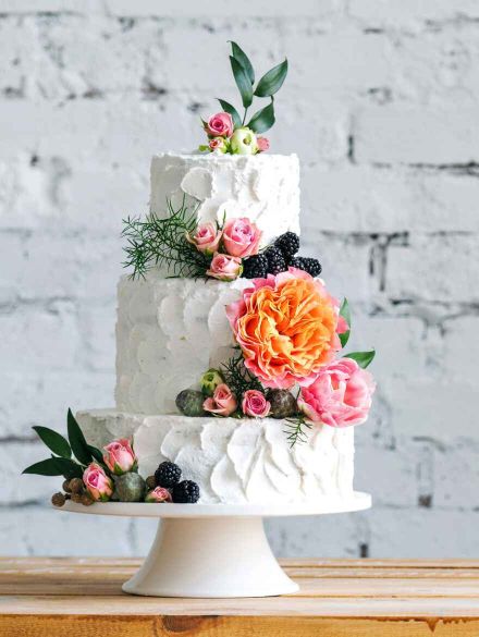A multi-tiered cake with smooth white frosting, adorned with fresh flowers and delicate piping.