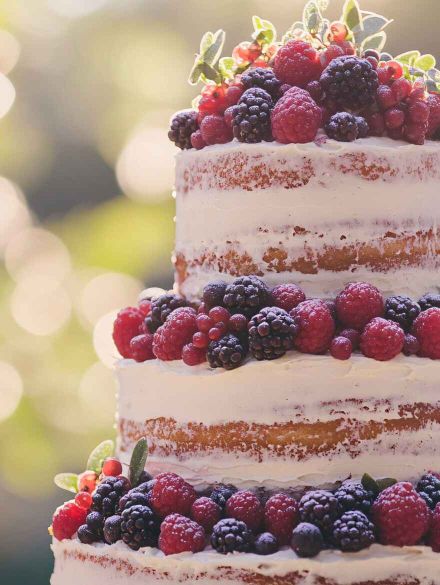 A "naked" cake with exposed layers, decorated with fresh berries and greenery for a natural feel.